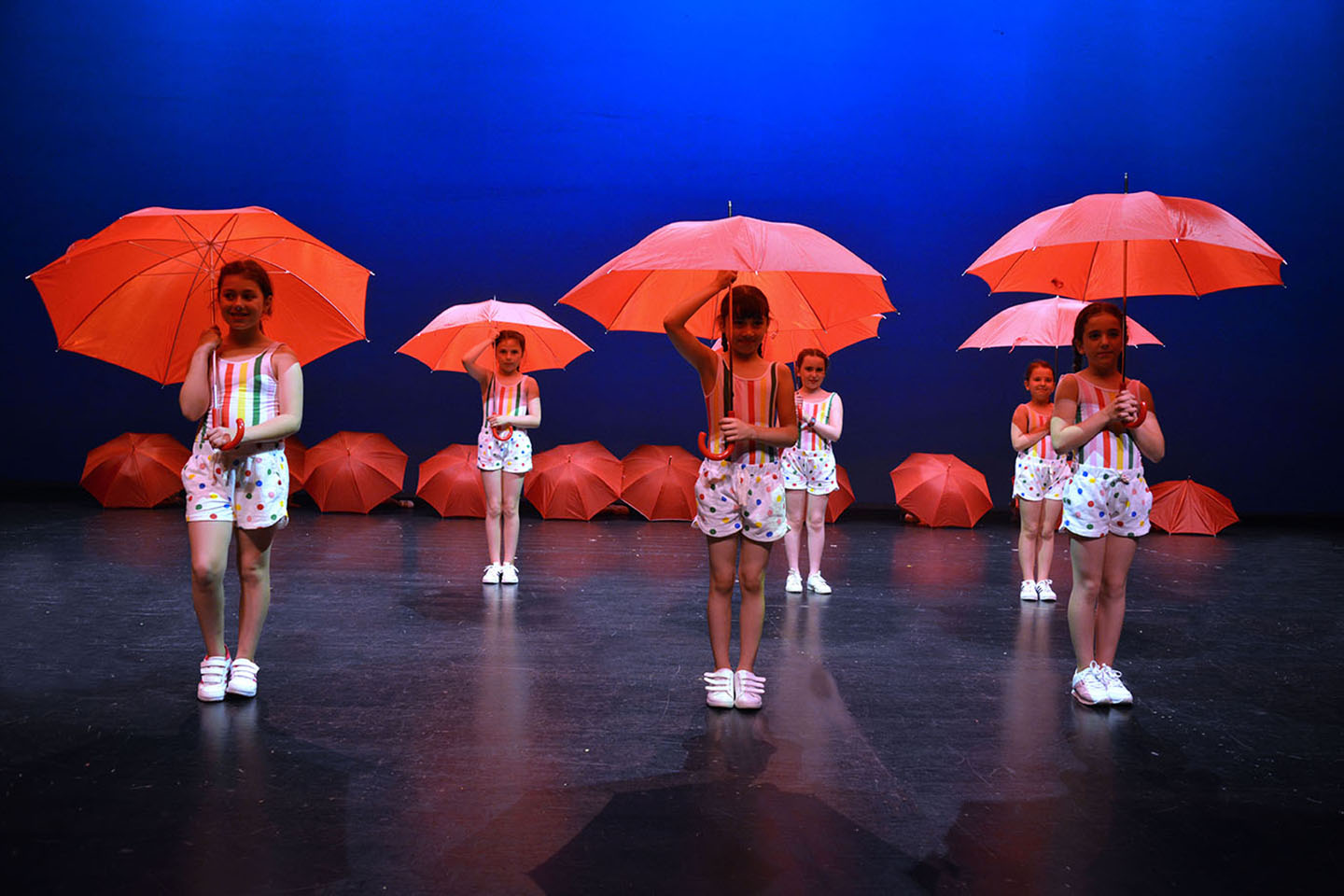 Baile de los paraguas rojos con niñas vestidas de llunares de colores